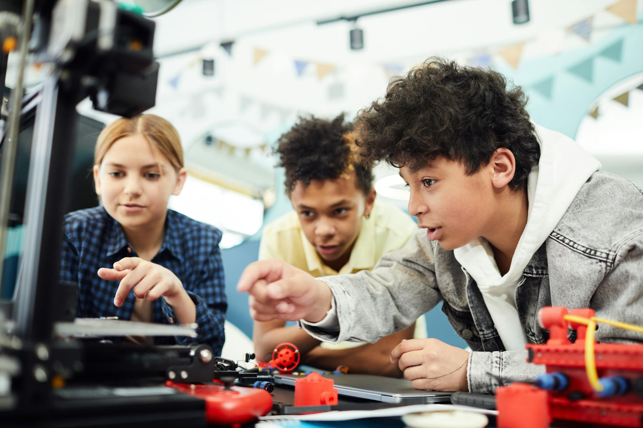 Three teenagers focused on a STEM project using a 3D printer in a collaborative indoor setting.